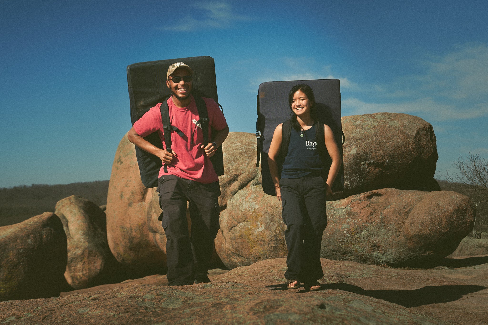 Two people wearing Rhyo / 02 shirts with bouldering crash pads on their back.