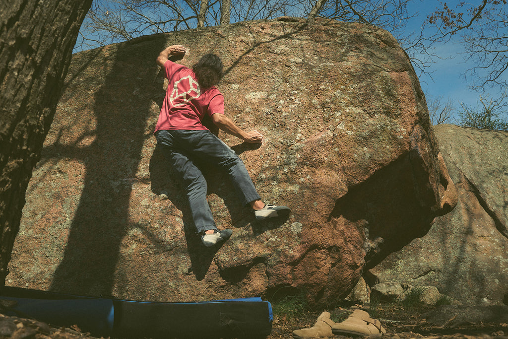 Person climbing a large rock wearing the Rhyo / 02: Process t-shirt.